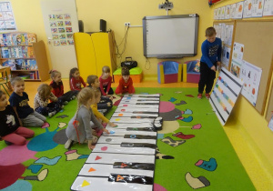 Chłopiec wskazuje kolejność granych dźwięków na tablicy muzycznej, troje dzieci odtwarzają dźwięki na instrumencie.